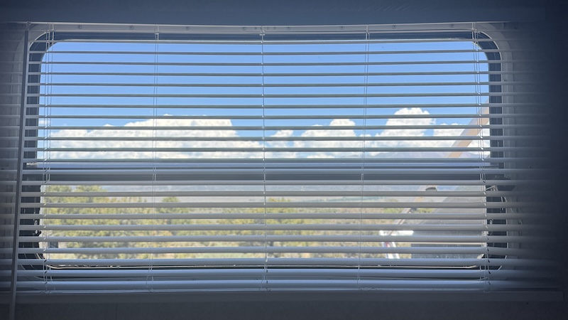 mini blinds on bedroom window—sky and landscape are seen through the slats.